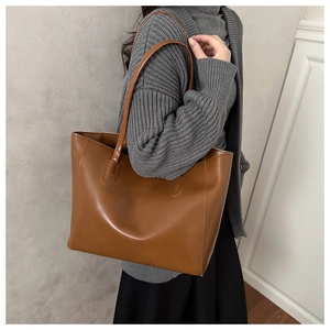 Detailed side view of a large brown leather tote bag worn by a model in a casual outfit