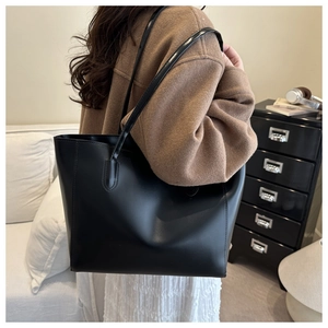 Minimalist black leather tote bag with large capacity shown on shoulder in a home setting