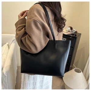 Minimalist black PU leather tote bag worn by model in a cozy, stylish room setting