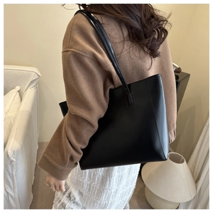 Detail view of a minimalist black leather tote bag featuring clean stitching and sleek strap
