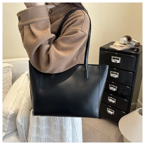 Chic black matte leather tote bag shown on model in a modern minimalist home setting