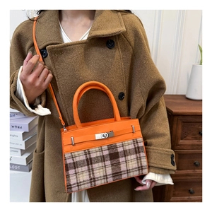 Detail van oranje lederen en geruite crossbodytas met metalen gesp en textuurafwerking