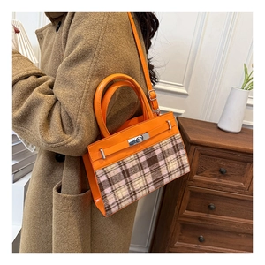 Detail van een vintage oranje geruite handtas met zilveren draaisluiting en leren greep