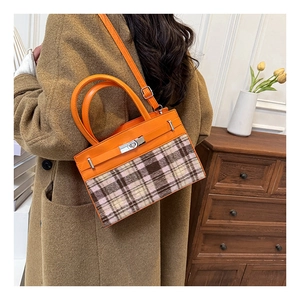 Detail van oranje leer en geruite tweed stiksels op een gestructureerde Kelly-tas met riem