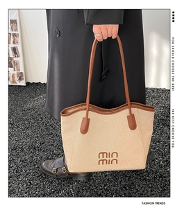 Detail of straw woven tote bag featuring brown leather trim and embroidered lettering logo