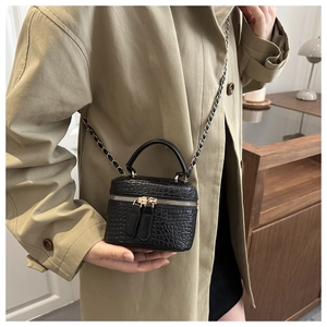 Close-up of black crocodile-embossed vanity box bag with gold zipper and chain strap