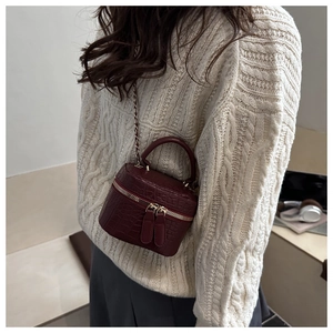 Detail of burgundy crocodile-embossed mini box bag with gold chain and handle
