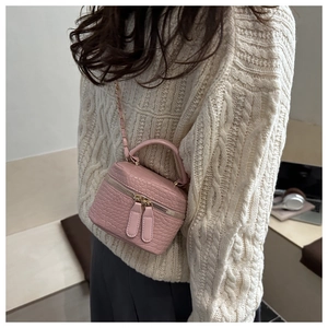 Detail of pink croc-embossed mini crossbody bag with gold chain and handle worn with sweater