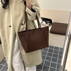 Minimalist dark brown leather tote bag worn by a model in a cozy urban setting