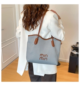 Detail of blue-grey woven tote bag with brown leather trim and metallic brand logo