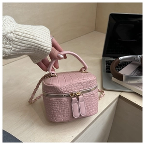 Macro detail of pink crocodile-embossed vanity bag showing dual zippers and chain strap