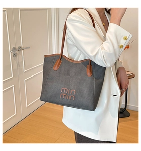 Detail of dark grey woven tote bag with brown leather straps and orange embroidery