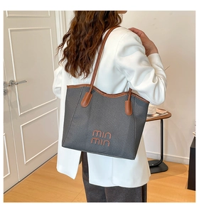 Detail of grey woven tote bag with brown leather handles and orange letter branding