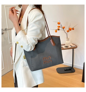 Detail of grey woven tote bag with brown leather strap and embroidered logo on shoulder
