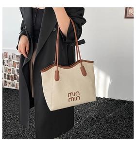 Close-up of beige canvas tote bag with brown leather trim and min min lettering