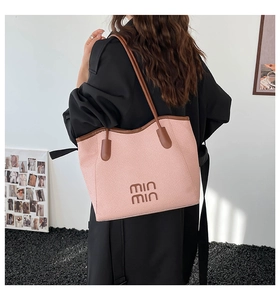 Detail of pink woven tote bag featuring brown leather trim and min min lettering