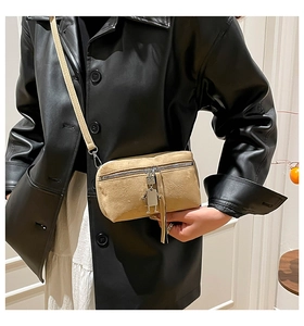 Detail of beige textured crossbody bag with silver zipper and robot charm on a model