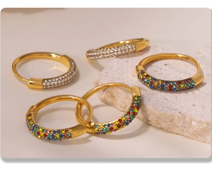 Close-up of four gold hoop earrings with colorful and white zircon inlay on stone surface