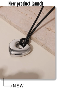Détail macro du pendentif cœur en acier poli sur un collier minimaliste en cordon noir