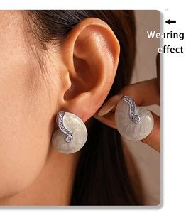 Close-up of elegant cream marble-textured stud earrings with silver borders on ears