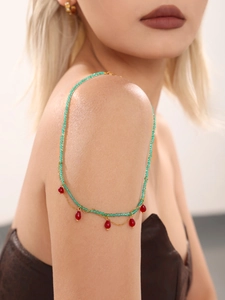 Detail of beaded necklace with green round beads and red teardrop pendants on shoulder