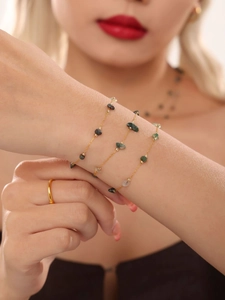 Detail eines mehrlagigen Goldkettenarmbands mit grünen Natursteinen am Handgelenk
