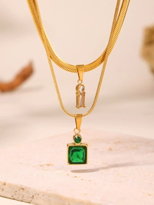 Macro detail of layered gold necklaces with emerald green and clear zircon pendants