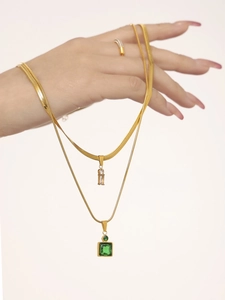Detail of layered gold stainless steel necklaces with green and clear square gemstones