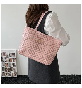 Sac fourre-tout rose à monogramme avec nœud doré porté à l'épaule par un mannequin