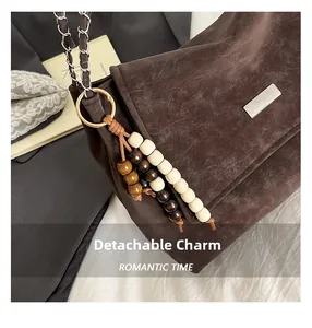 Detail of dark brown suede crossbody bag featuring wooden bead charm and metal chain