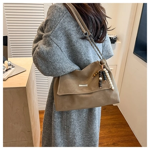 Detail of khaki tote bag featuring beaded charm and textured soft leather finish