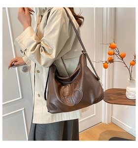 Dettaglio borsa hobo vintage marrone con logo in rilievo indossata da una modella
