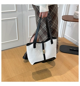 Close-up of white croc-embossed tote bag with black handles and golden metal buckle