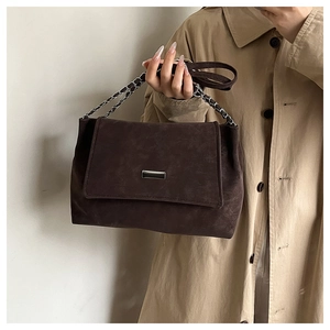 Detail of dark brown matte suede shoulder bag with minimalist silver metal buckle