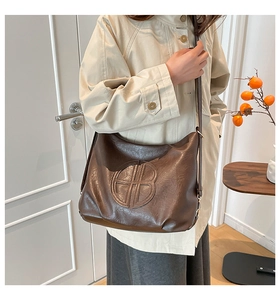 Detail of dark brown leather shoulder bag featuring a circular embossed logo on front