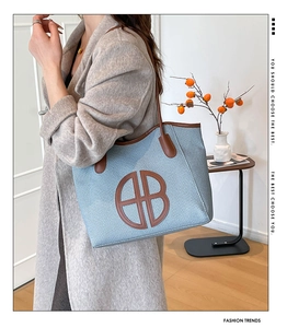 Detail of blue woven tote bag with brown leather handles and cutout logo decoration
