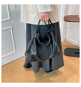 Detail of a black leather tote bag with circular embossed logo and adjustable strap