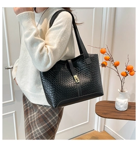 Detail of black woven texture tote bag featuring a gold rectangular metal clasp and long straps