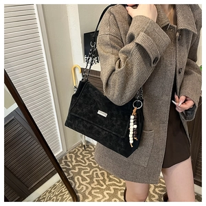 Detail of matte black crossbody bag with metal chain strap and bohemian bead charm