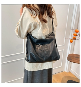 Detail of black large capacity hobo bag featuring a circular embossed logo and metal hardware