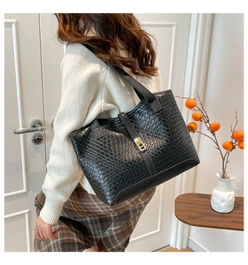 Detail of black faux leather tote bag with crocodile pattern and gold metal buckle