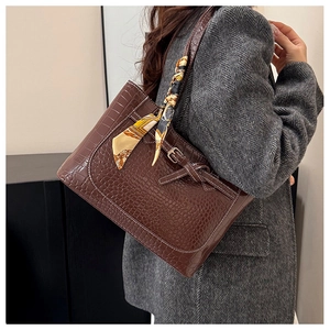Detail of dark brown croc-embossed tote bag with white stitching and floral scarf handle
