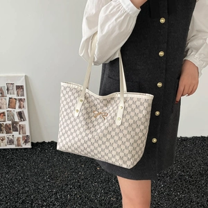 Sac cabas beige avec motifs de lettres marron et nœud doré porté par un modèle