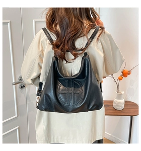 Detail of the black leather shoulder bag with circular geometric embossing on a female model
