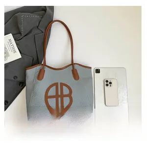 Detail of grey-white woven tote bag with brown leather handles and circular logo patch