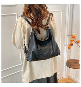 Detail of black faux leather tote with embossed logo and golden hardware on model