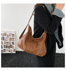 Macro detail of brown leather hobo bag featuring embossed round logo and gold hardware