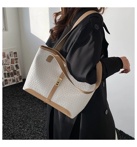 Detail of woven tote bag featuring light brown leather trim and golden metal turn-lock
