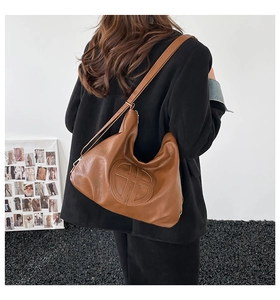 Detail of a brown leather bag showing the round 3D logo and adjustable wide strap