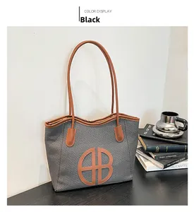 Close-up of black and grey woven tote bag with brown leather handles and logo on a table